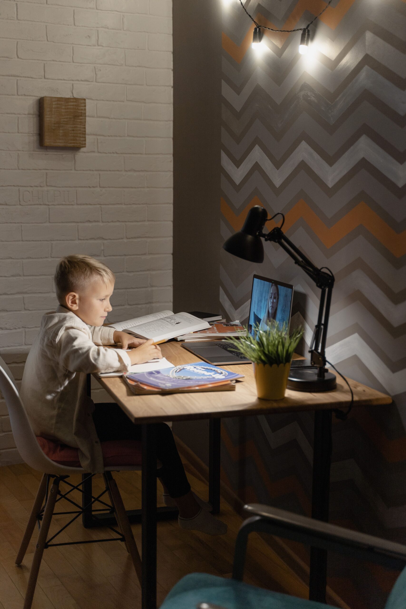 Young boy focused on online class at home, with books and laptop.